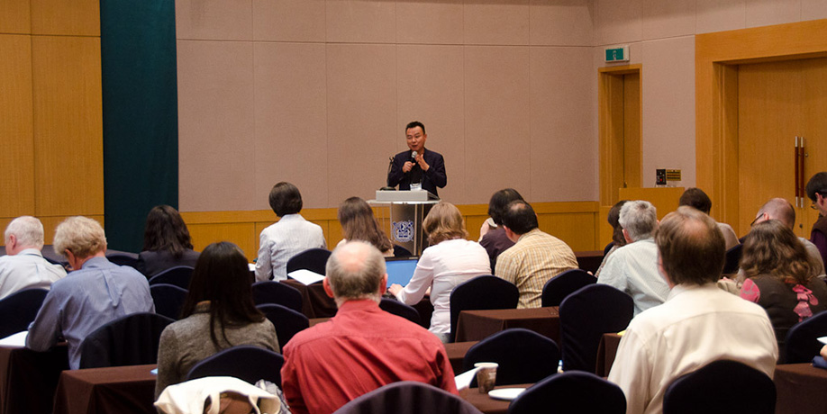 A man standing at a podium speaking to a group of conference attendees in a lecture hall