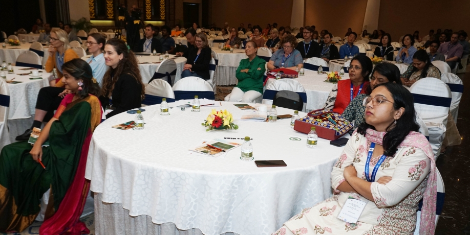 Attendees sit at tables with white tablecloths and listen to a speaker