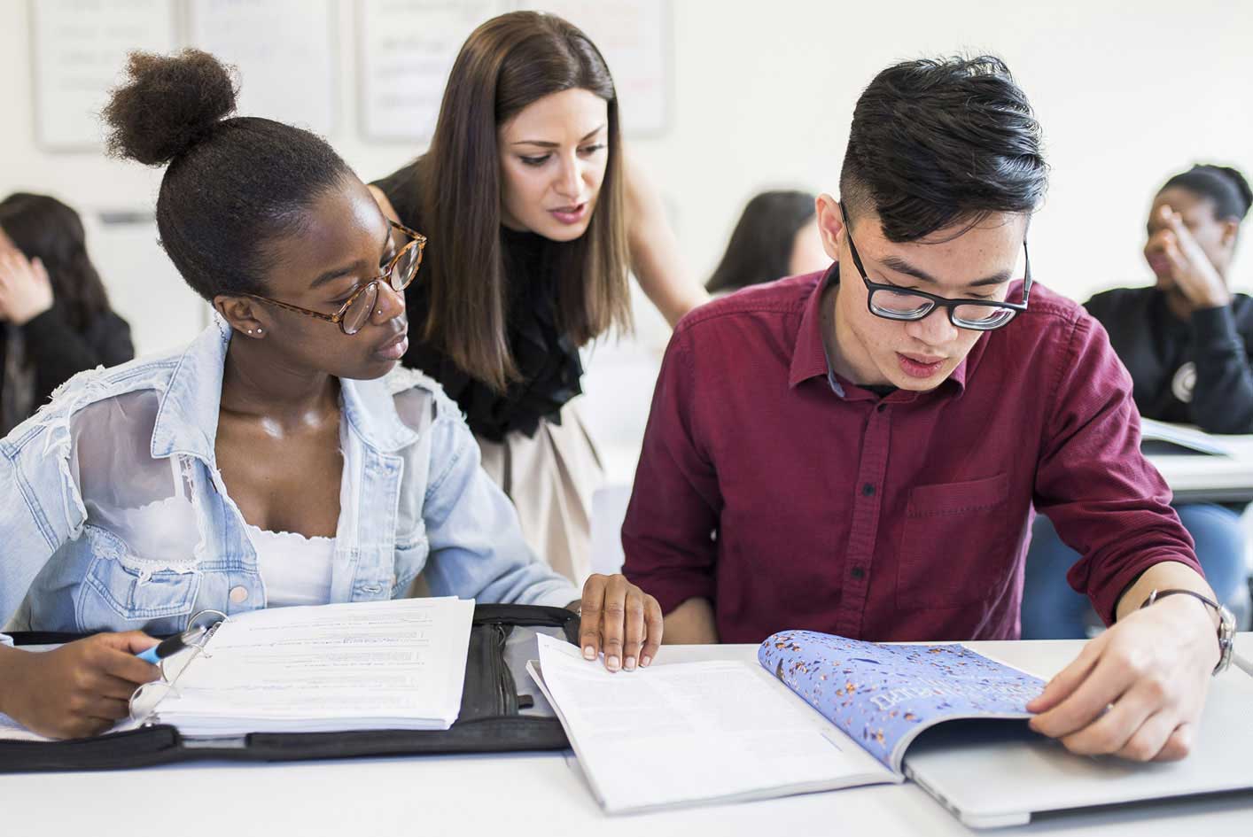 a Black female student and an Asian male student studying together with a white female instructor overseeing them