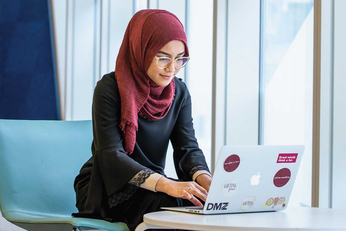 a female student wearing hijab typing on a laptop