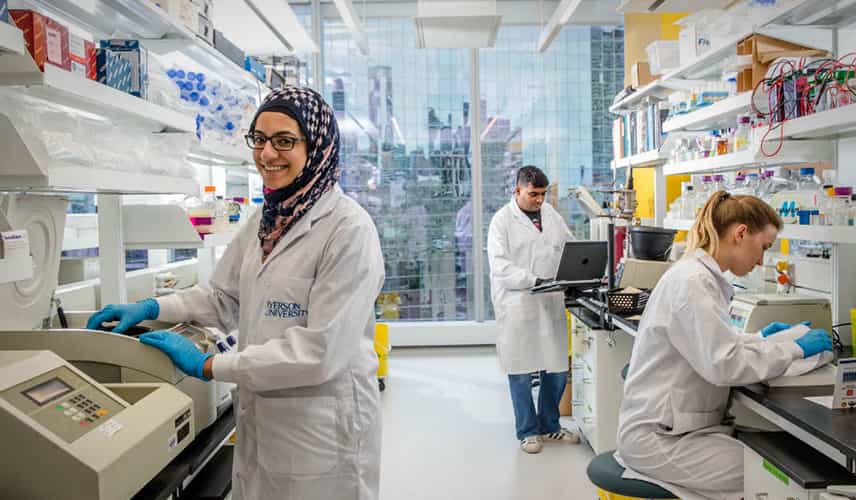 three students in a science lab, with a female student wearing a hijab at the front