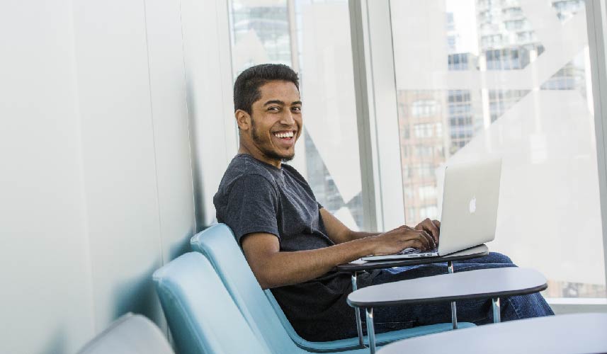 A student is seated inside the SLC doing his work and smiling at the camera.