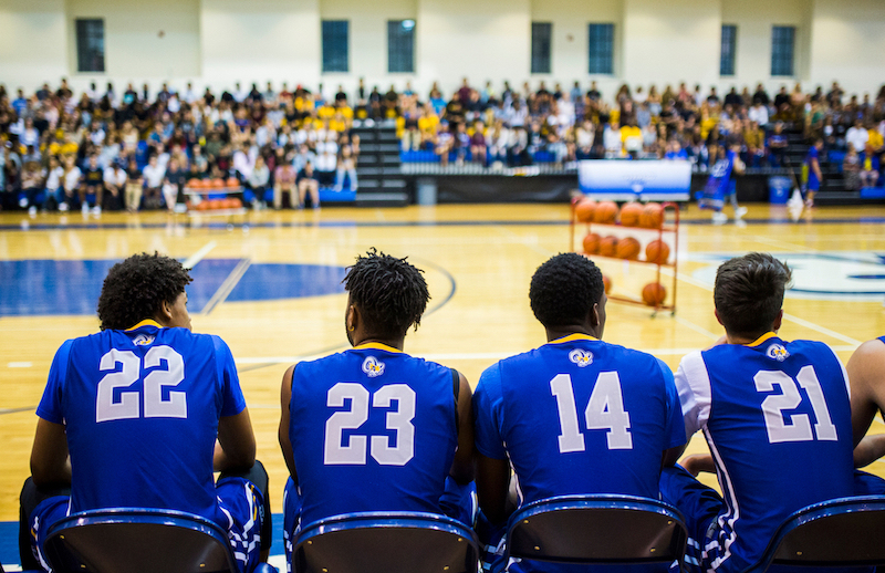 Four TMU athletes are seated in front of the game court. Audience can be seen in the background.