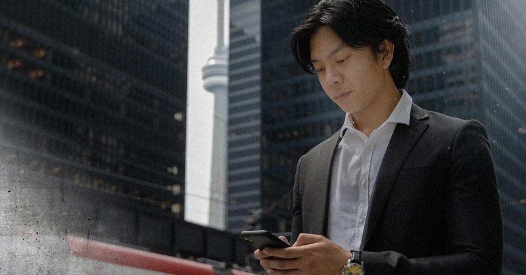 Professionally-dressed student checking their phone in downtown Toronto.