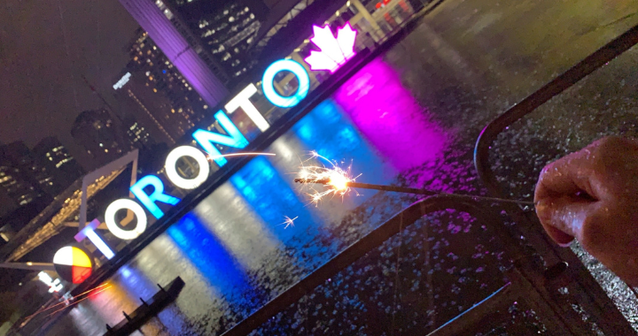 Priya holding a sparkler, Toronto sign at City Hall is seen in the background.  
