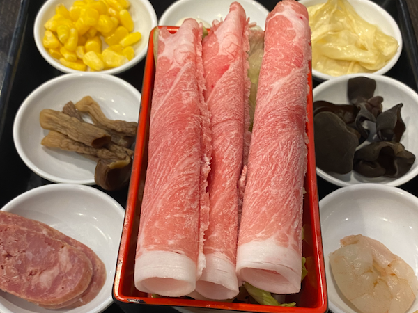 A tray of rice noodle toppings with shrimp, corn and various meats