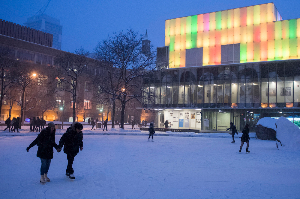 students ice skating at Lake Devo in the winter. There is snow on the lake and two students can be seen holding hands while ice skating.