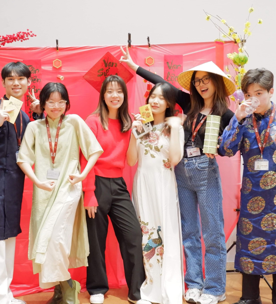 Students posing in front of a red Lunar New Year backdrop, wearing Vietnamese traditional clothing and holding festive props