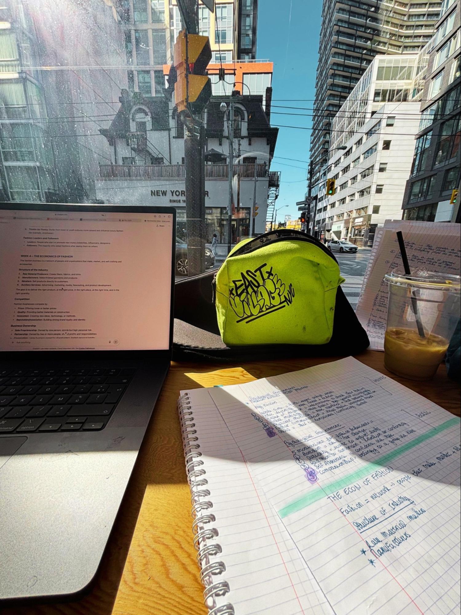 Study setup at cafe window overlooking Toronto street with laptop displaying notes