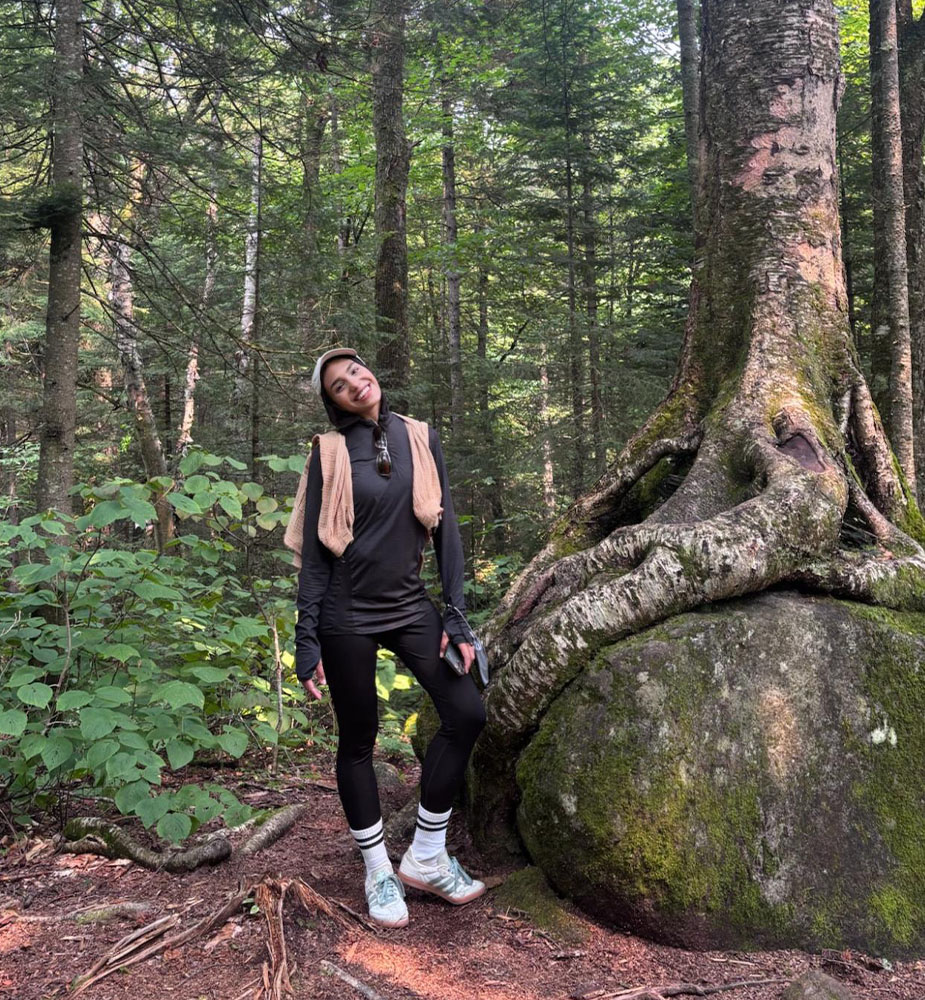 Safia posing by a mossy rock in the woods.