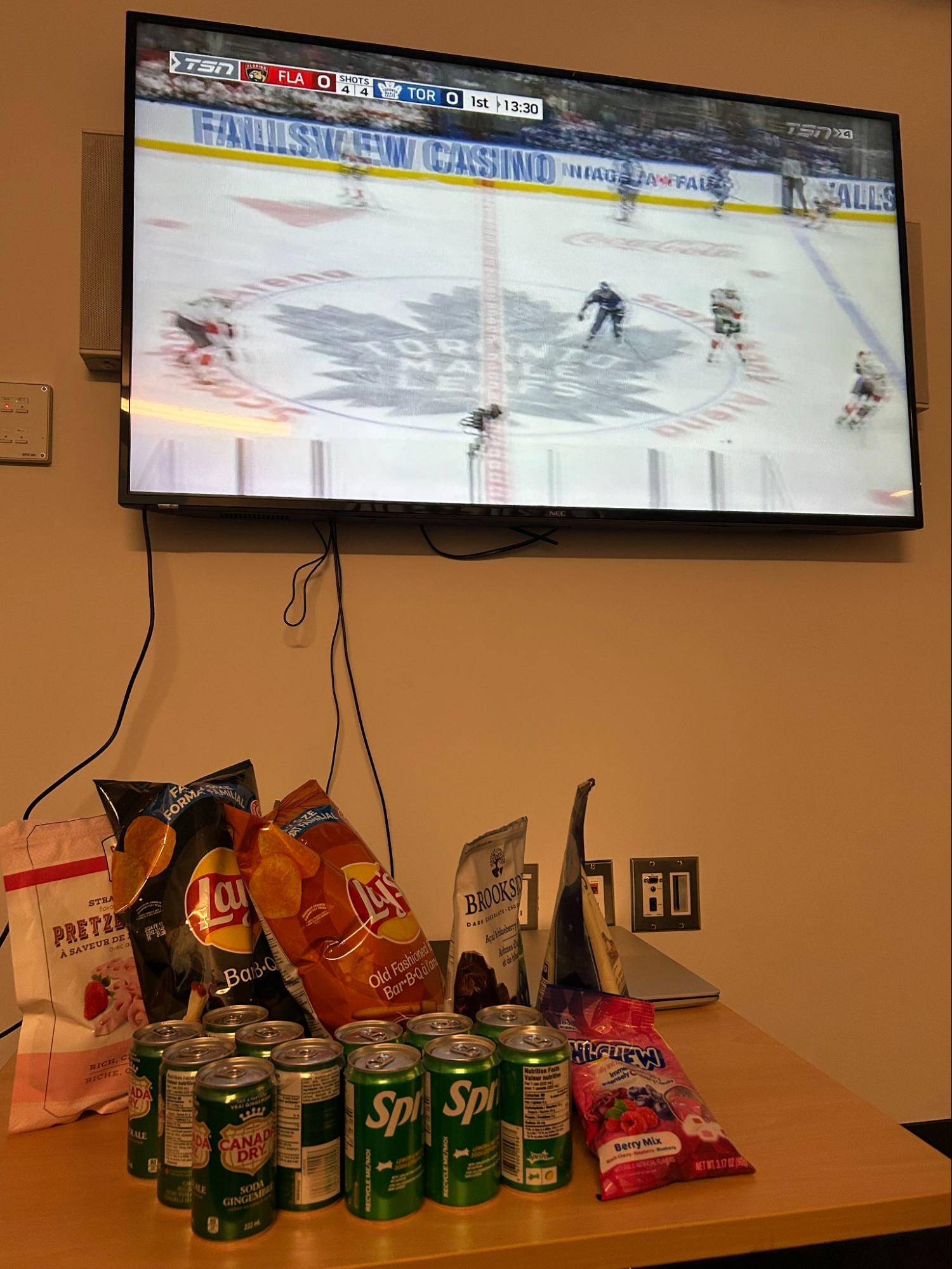 Snack setup with chips and drinks on a table in front of a TV showing a hockey game