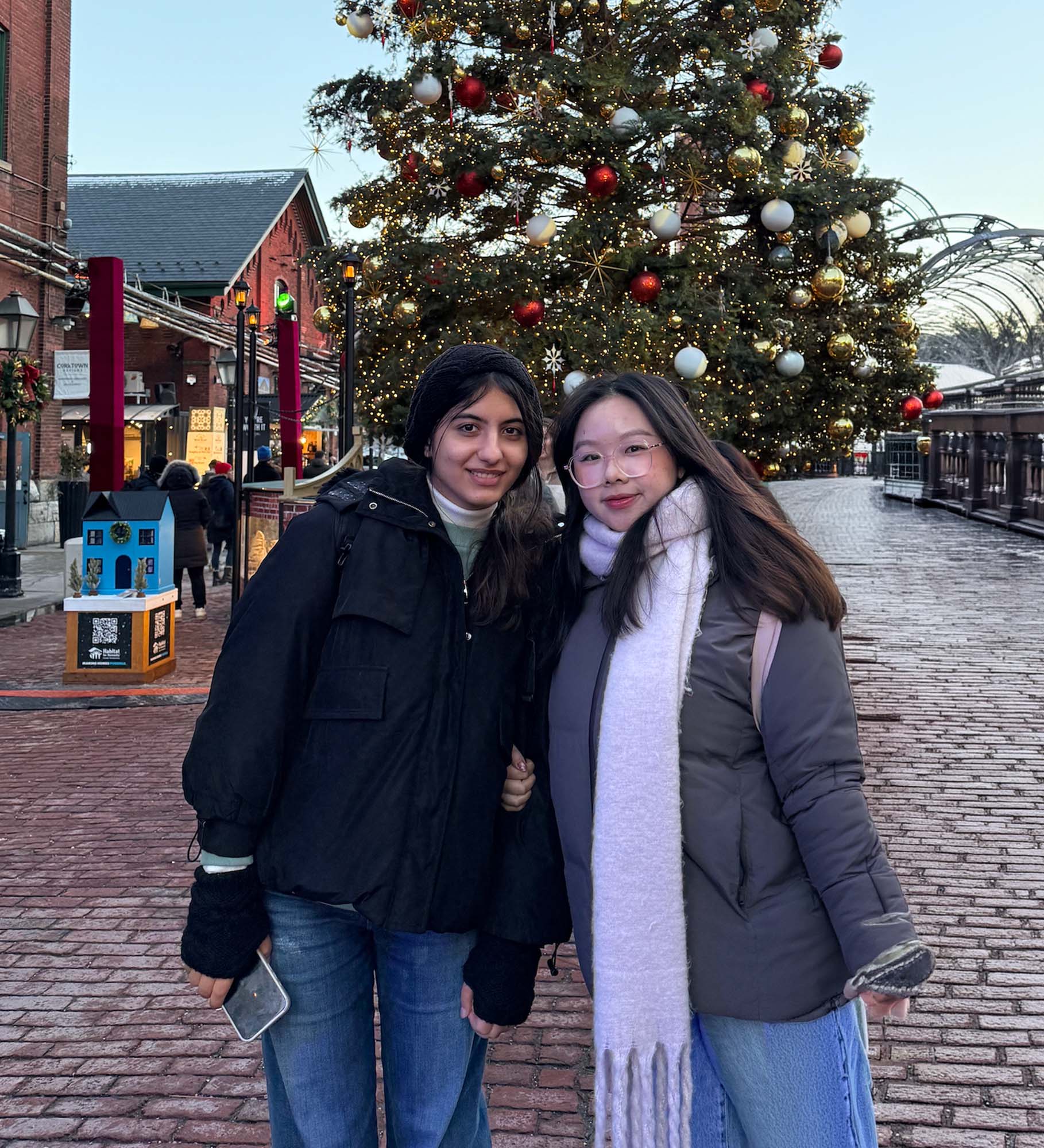 Julie and her friend posing in front of a decorated Christmas tree outdoors