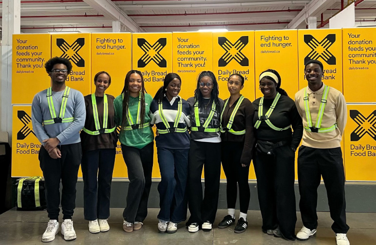Eight volunteers in neon green safety vests standing together in front of Daily Bread Food Bank signage at a volunteer event