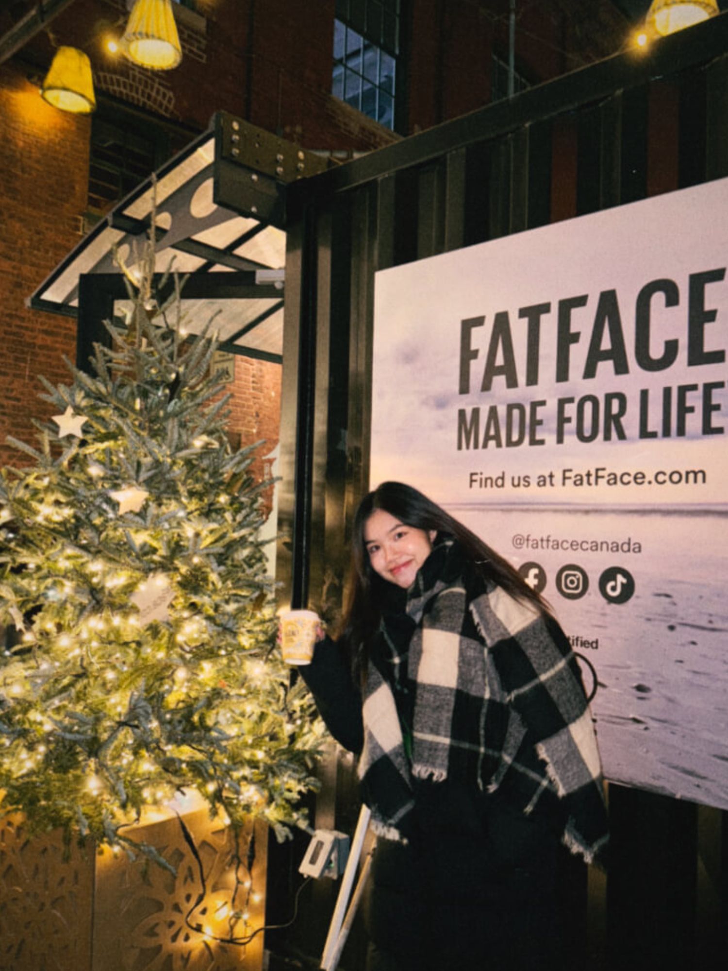 Student posing smiling next to a christmas tree at a outdoor christmas market