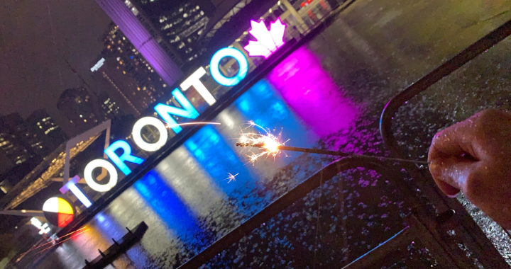 Priya holding a sparkler, Toronto sign at City Hall is seen in 
the background.  
