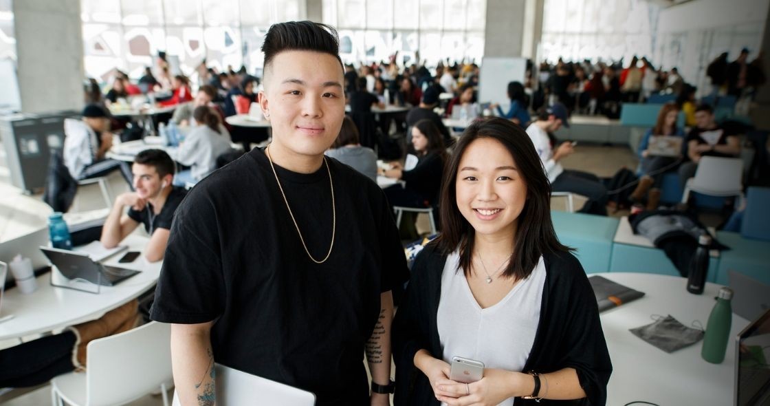 Two students smiling, standing in the Student Learning Centre