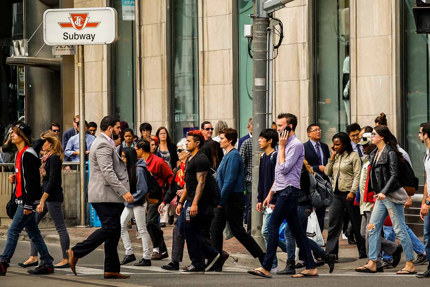 a bustling intersection in downtown Toronto with a diverse crowd crossing