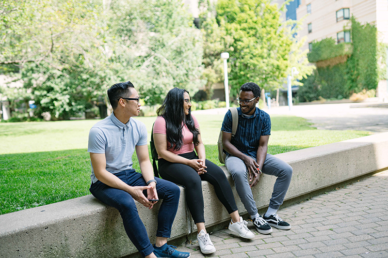 3 students sitting outside of the TMU quad.