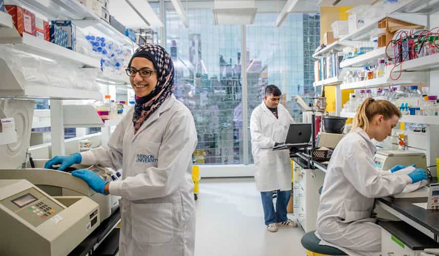 Three students in a science lab, with a female student wearing a hijab at the front