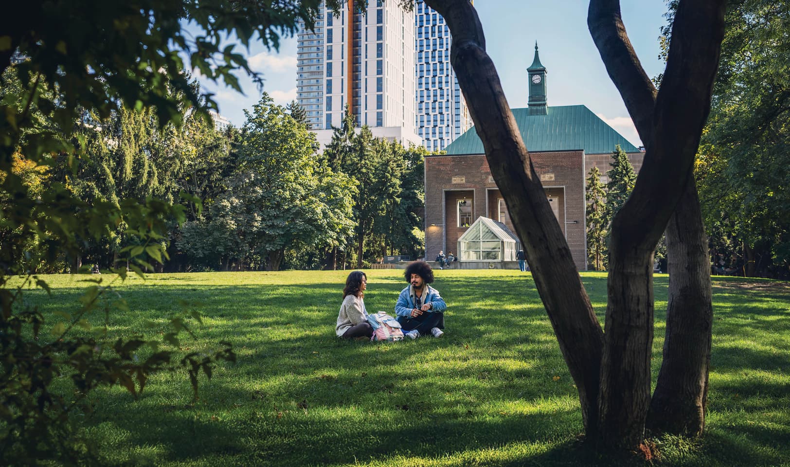 Two people sitting and talking on the lawn of the TMU campus quad on a sunny day.