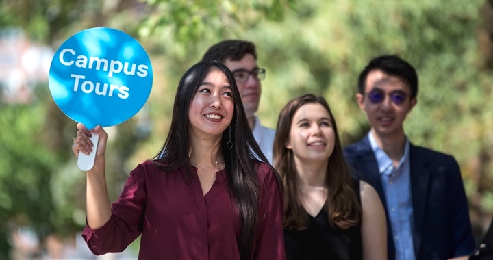Student Ambassador holding a Campus Tour sign as she leads a group through campus