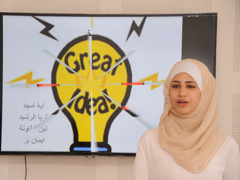 A female student stands in front of a screen delivering a presentation.