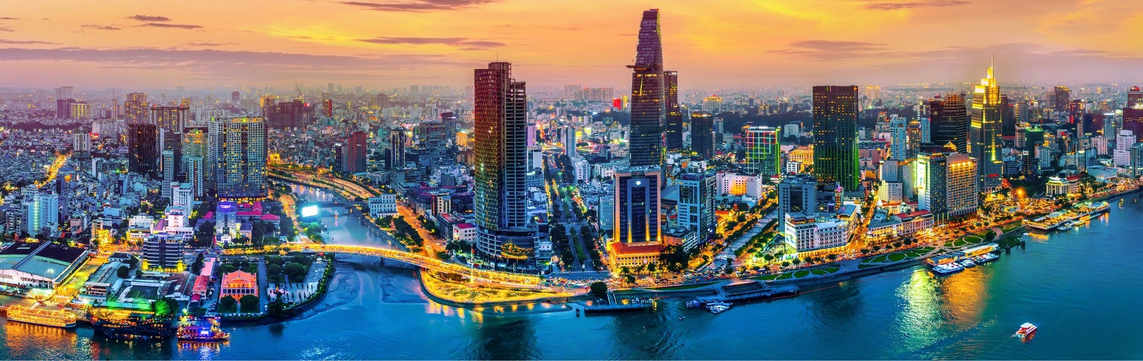 Aerial view of downtown Toronto at sunset, featuring the CN Tower, Lake Ontario, and a dense cluster of high-rise buildings illuminated by the evening light.