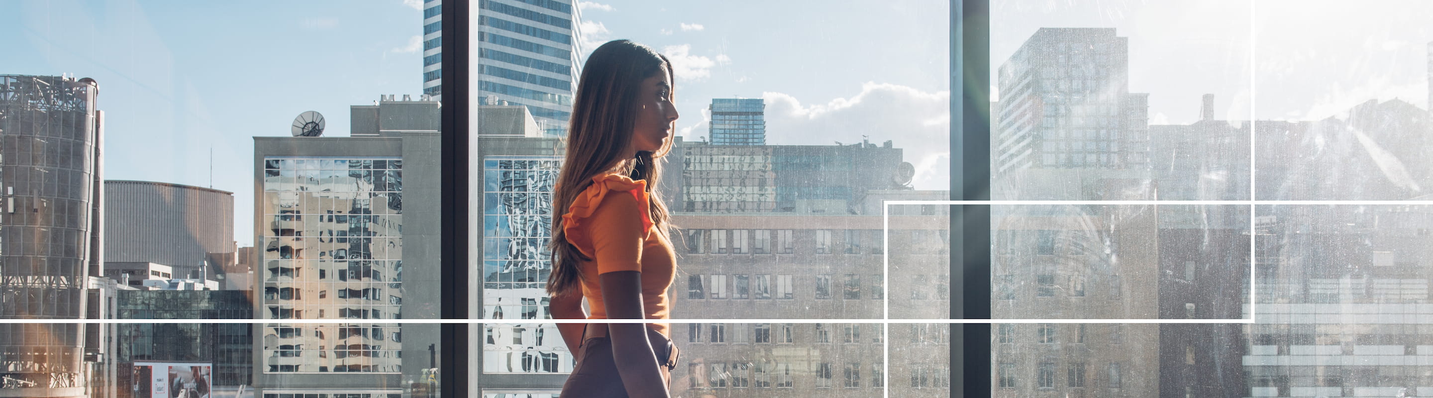 a female student standing in front of floor to ceiling windows with tall buildings in the background