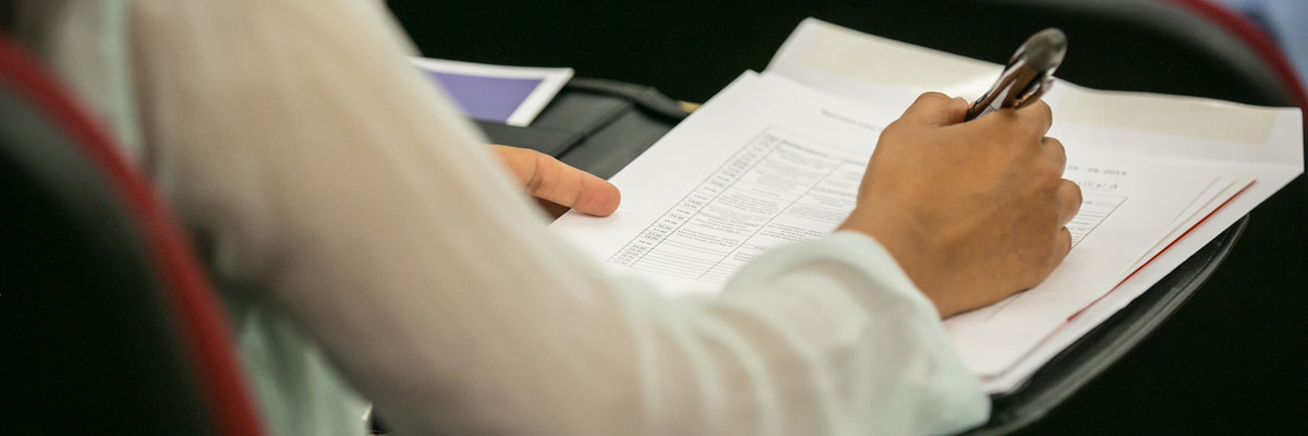 A woman's arm is poised to write with a pen on a white paper.