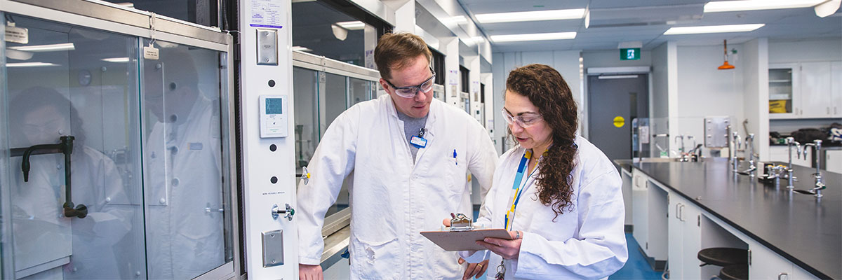 Inspectors in lab coats examine the fume hoods in a chemistry lab.