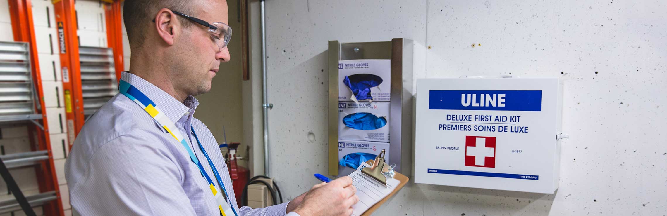 A man wearing safety glasses checks the first aid kit and stock of rubber gloves to in a workshop..