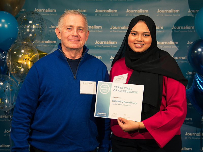 Nishat Chowdhury holds a certificate while standing with Scott Lauder in front of a blue backdrop that repeats, "Journalism at The Creative School."