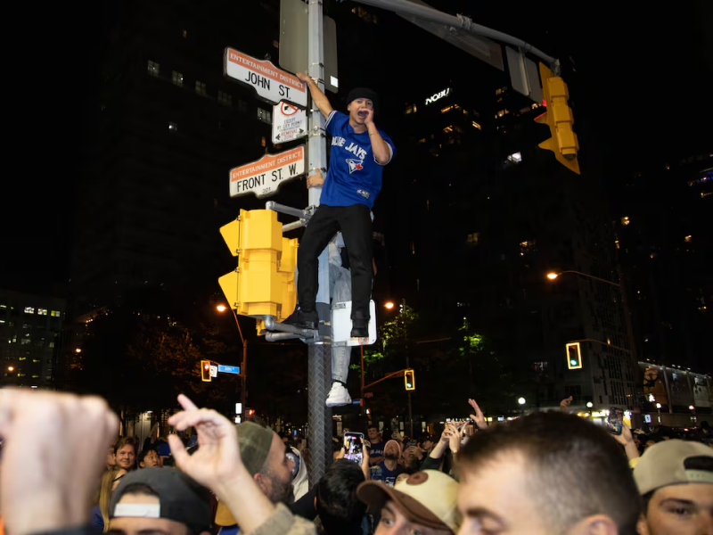 A man climbs a intersection light pole while shouting to a crowd below.