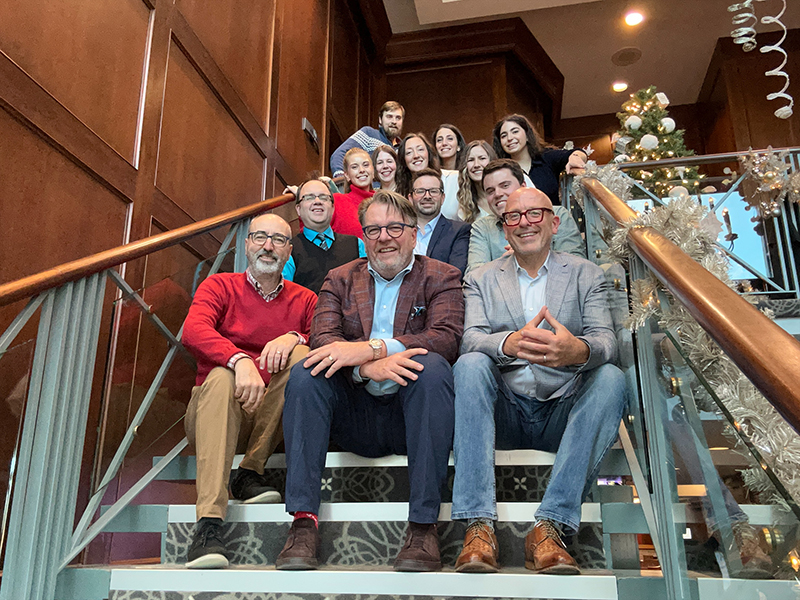 Photo of a group of people sitting up sets of stairs while smiling at the camera.