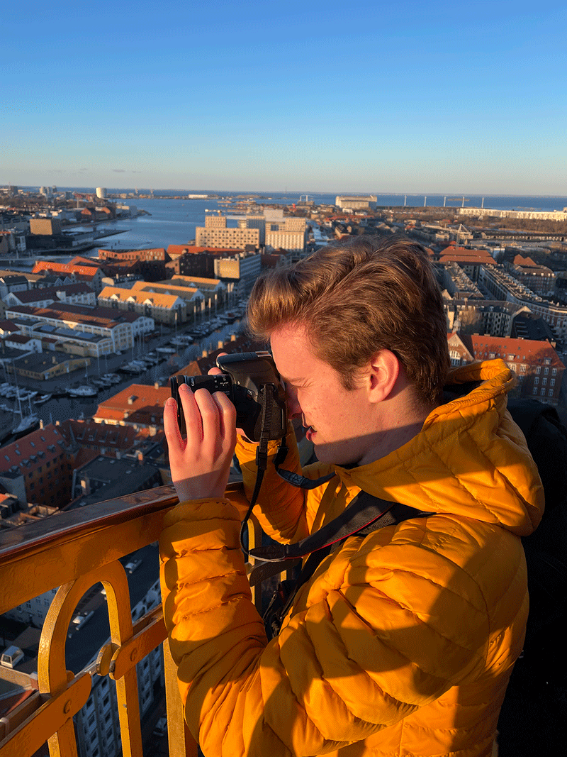 Caelan Monkman taking a photo standing on a bridge overlooking a city in Denmark