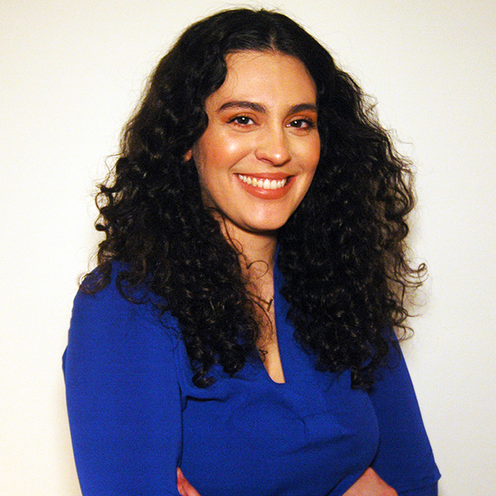 Head shot of Touria Izri. She is wearing a blue top against a white background.