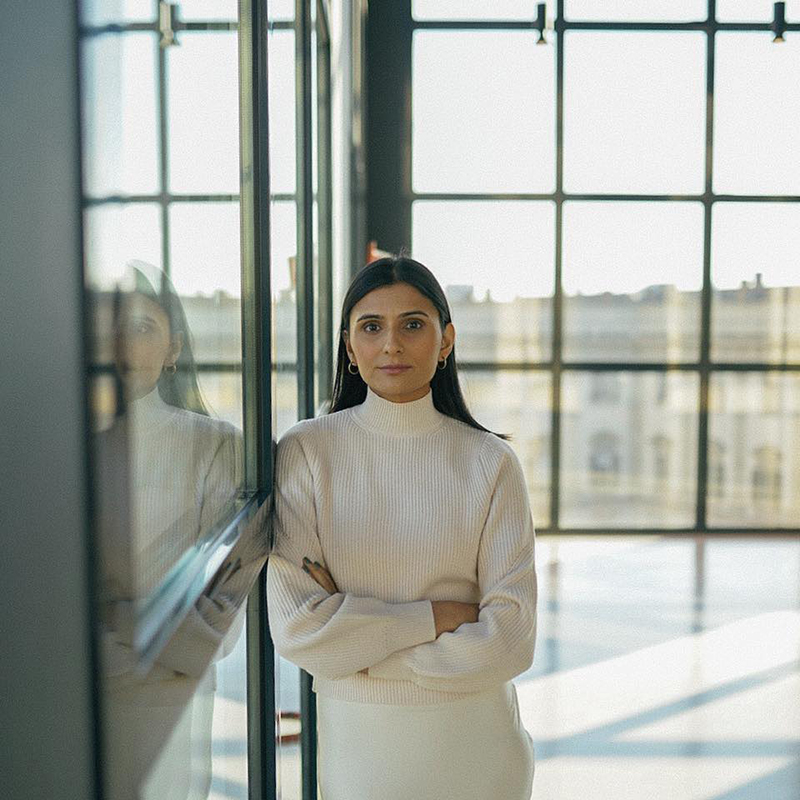 A headshot of Sabina Sohail standing in glass window-filled building