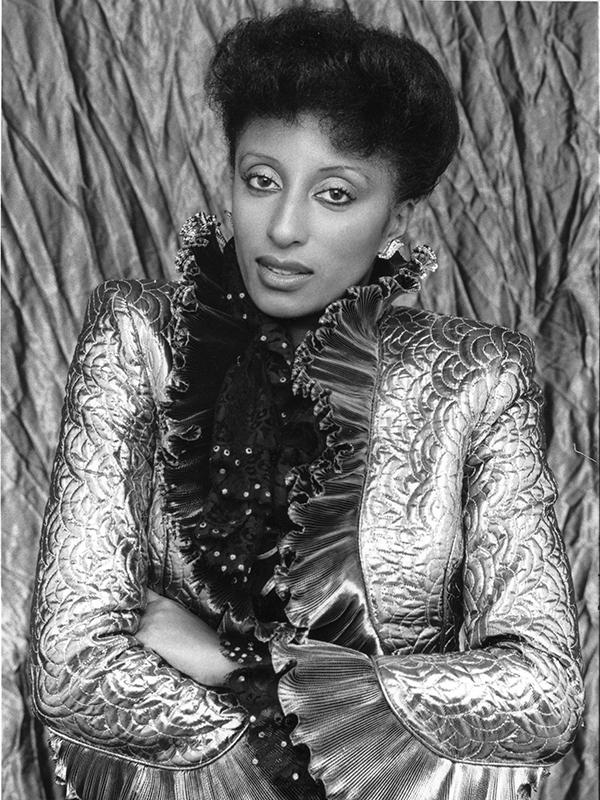 Linda V. Carter posing in a gold jacket with dramatic frills. Photo taken by Hans Lichenberg.