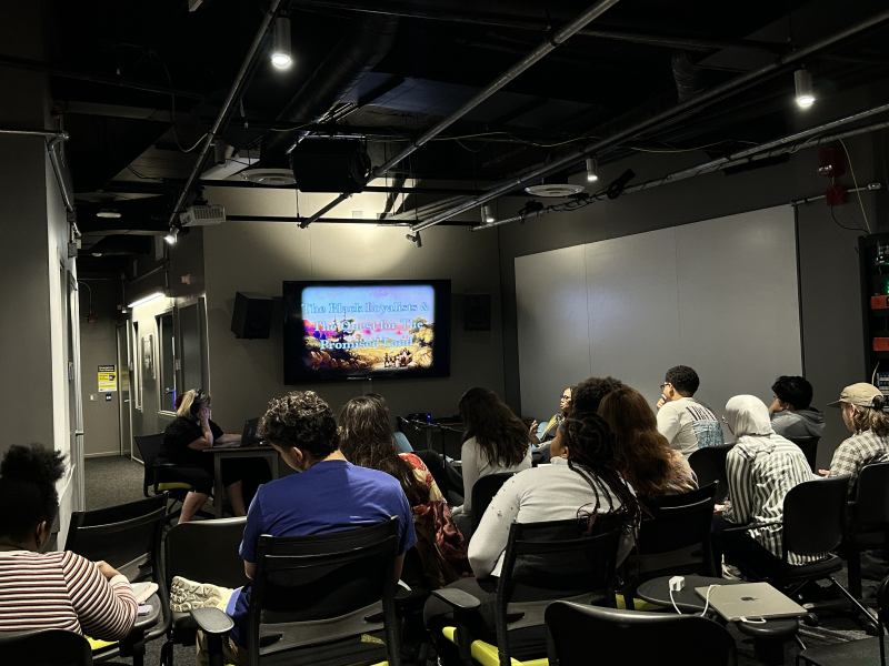 Students sit in rows while watching Journalism professor Shari Okeke chats with podcaster Nichole Hill during a podcast recording.