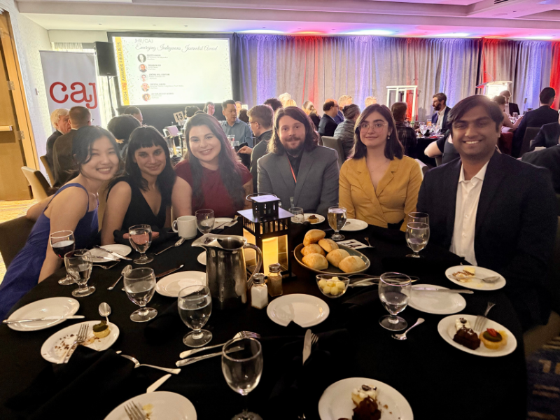 A group of six young adults at a gala sit next to each other around a table