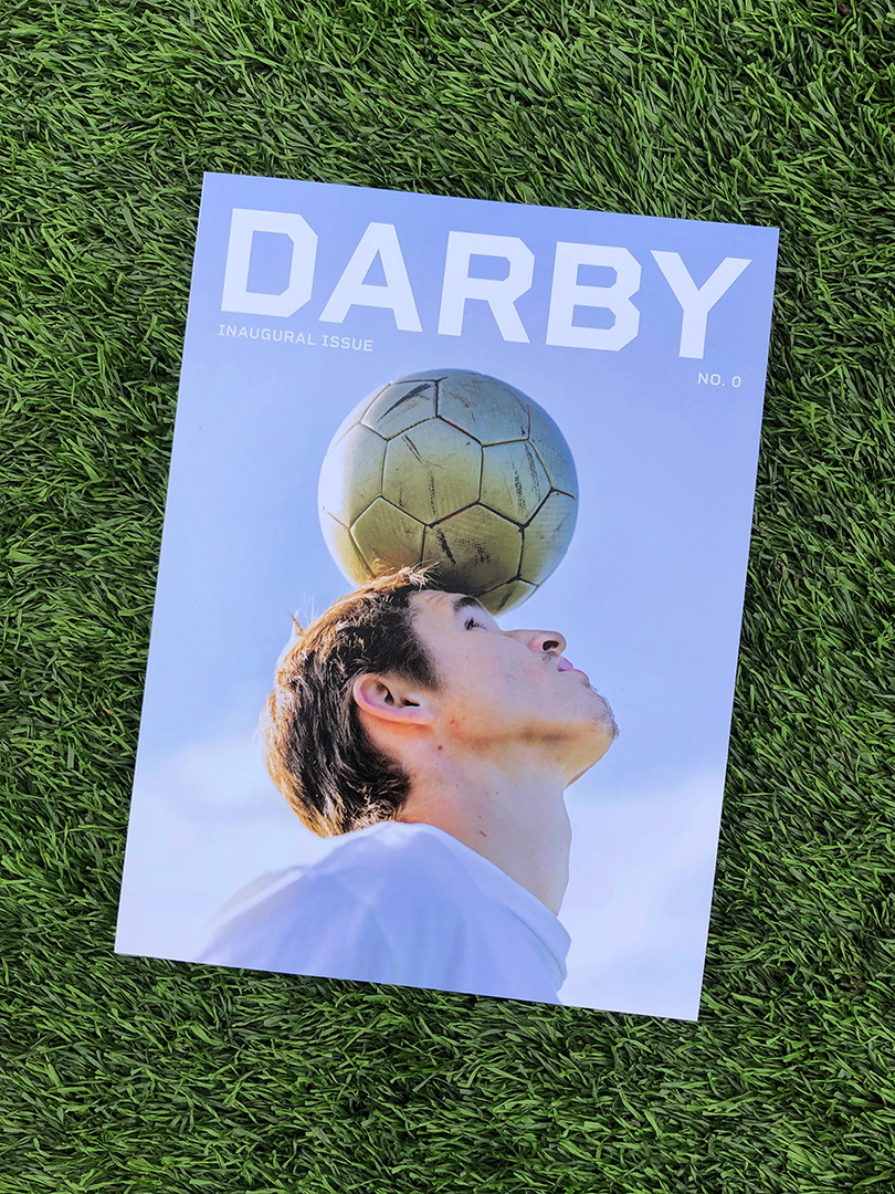 An issue of Darby magazine on the grass. A soccer player balances a ball on his head for the cover shot.