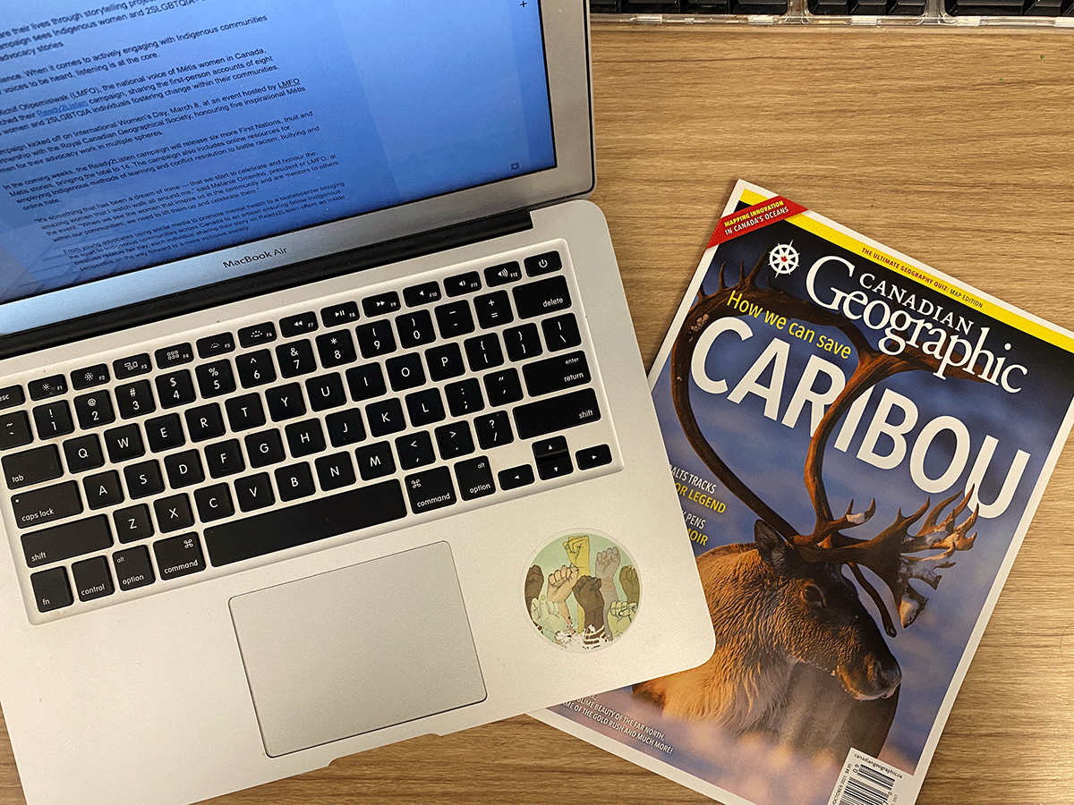 A laptop on a desk with a copy of National Geographic magazine