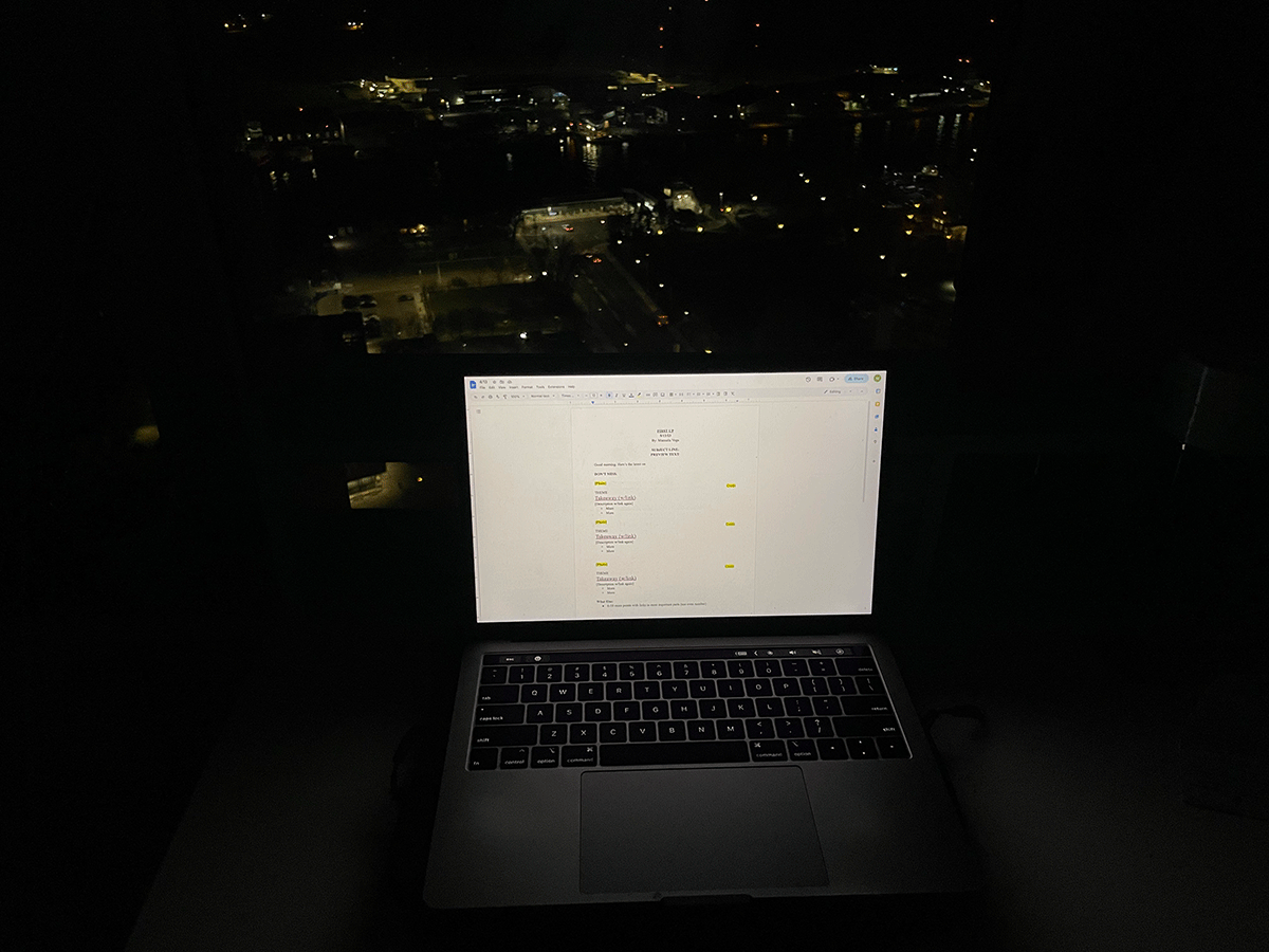 A laptop sitting on a desk with a view of the city of Toronto before the sun rises.