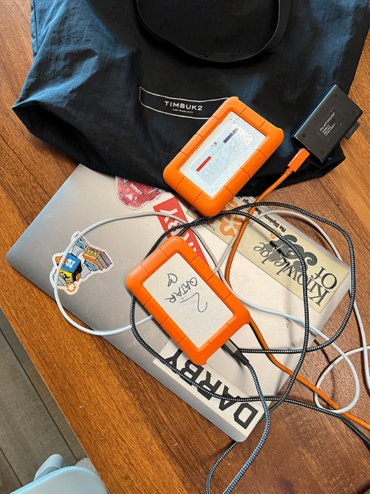 A closed laptop, two orange hard drives and a backpack sitting on a desk