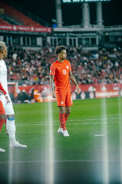 A soccer player in a red jersey stands on the field at BMO field.