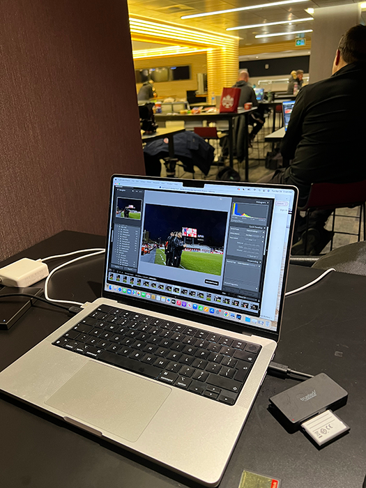 A laptop showing photo editing software sitting on a desk in a busy media room.