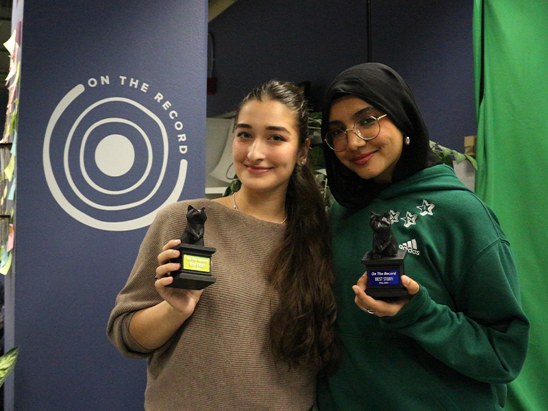 Two students hold awards up while smiling at the camera.