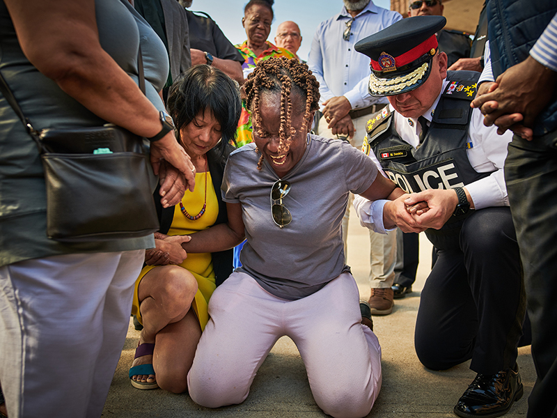 A person kneels on the ground screaming while being held up by two people.