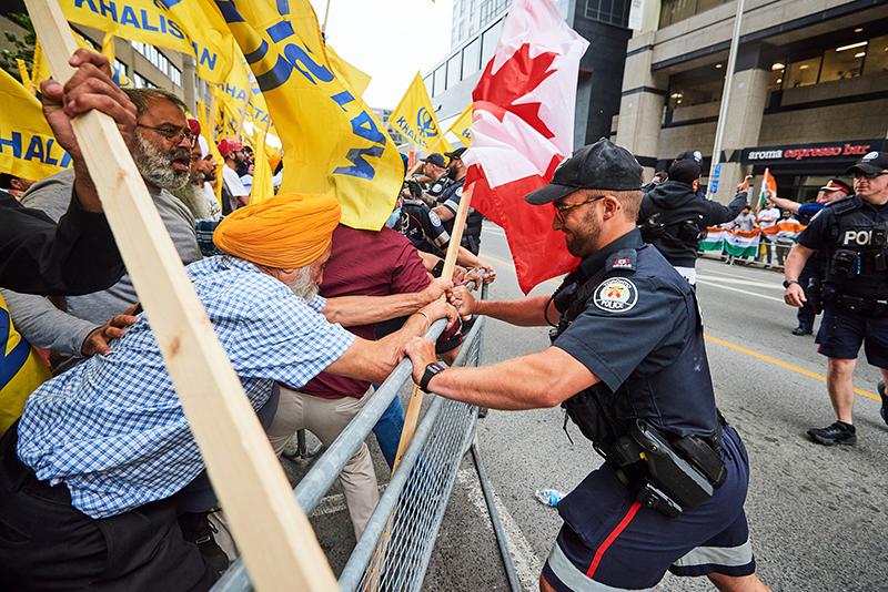 A police officer on one side of a fence pushing it in while a group of people with yellow flags push back.