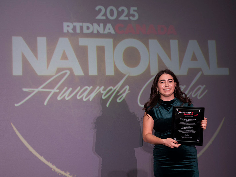 Photo of a person holding an award plaque in front of a gala sign